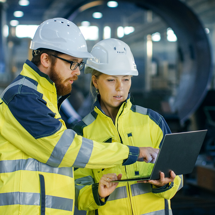 two individuals in the workforce with hard hats on and wearing reflective clothing