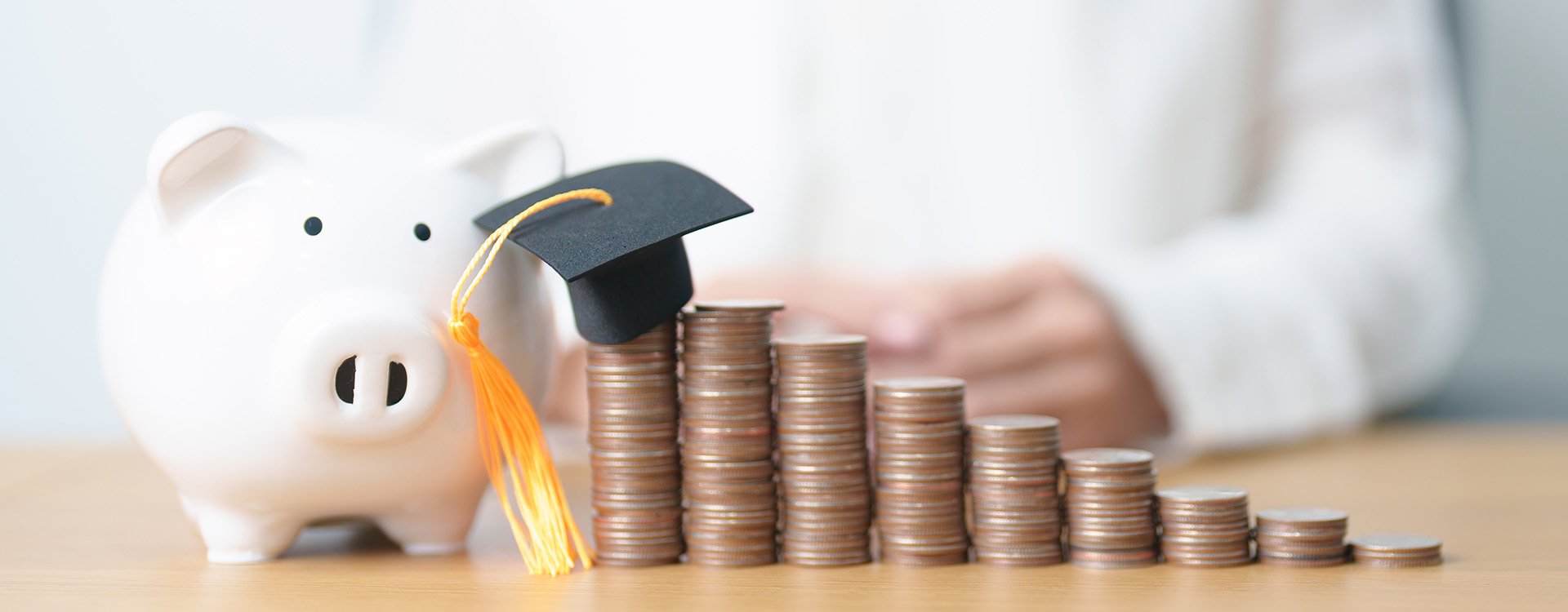 an increasing stack of coins from the right leading to a piggy bank and graduation cap