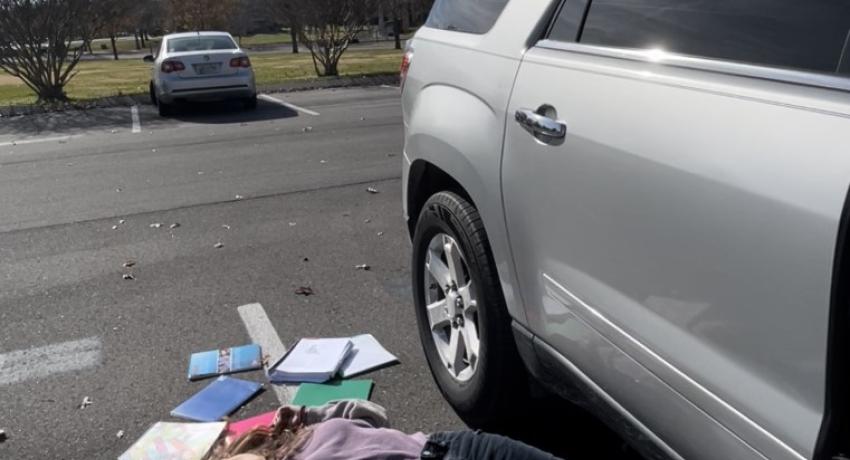 student laying next to car with her class books and notes scattered on the ground
