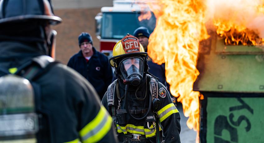 two fire personnel recruits practice putting out a dumpster fire